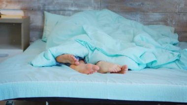 Battaniyenin altında erkek ve kadın ayakları görünüyor.