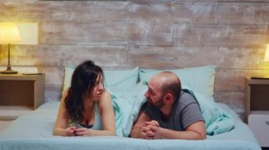 Genç çift pijama giyerek yatakta yatıyor.