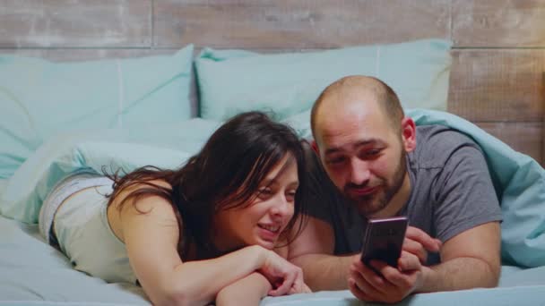 Wife in pajamas laughing while her husband is showing something on phone — Stock Video