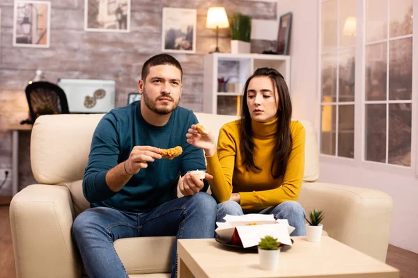 Jovem casal comer frango frito na frente da TV — Fotografia de Stock