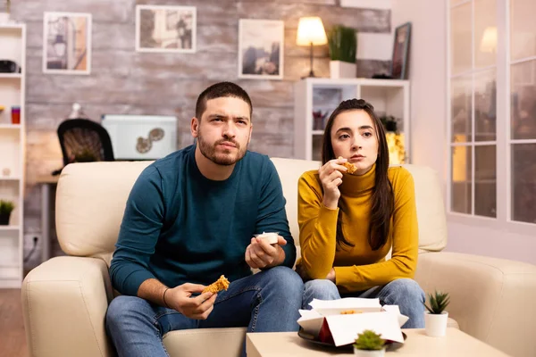 Молодая пара ест жареную курицу перед телевизором — стоковое фото