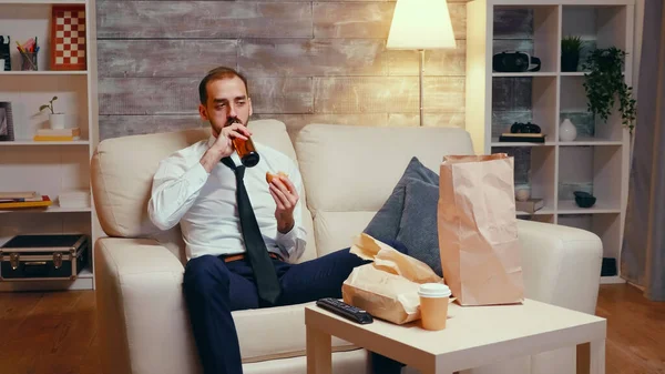 Businessman in suit sitting on couch eating a burger — Stockfoto