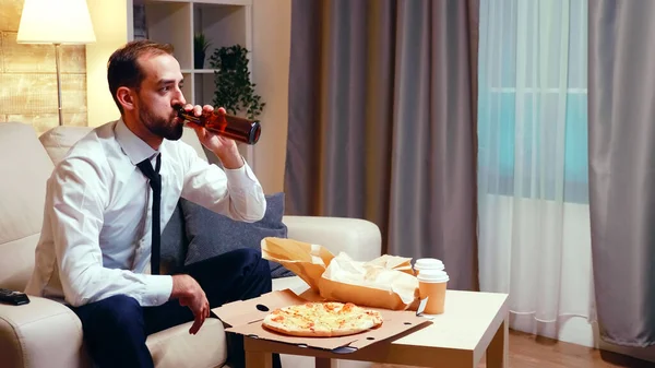 Бизнесмен отдыхает на диване, пьет пиво и ест пиццу. — стоковое фото
