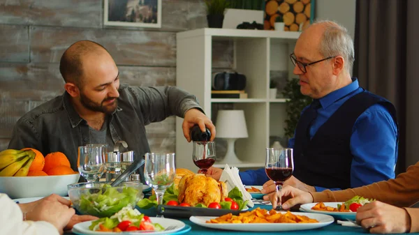 Young man serving his father in law with red wine