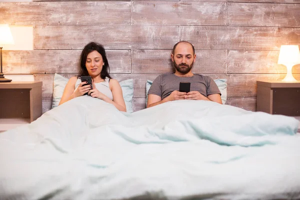 Кавказька пара у піжамі відпочиває за допомогою смартфона. — стокове фото