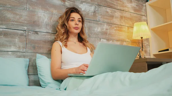 Кавказька жінка в піжамі читає онлайн статтю на своєму ноутбуку. — стокове фото