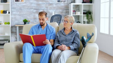 Huzurevinde emekli yaşlılara kitap okuyan erkek asistan.