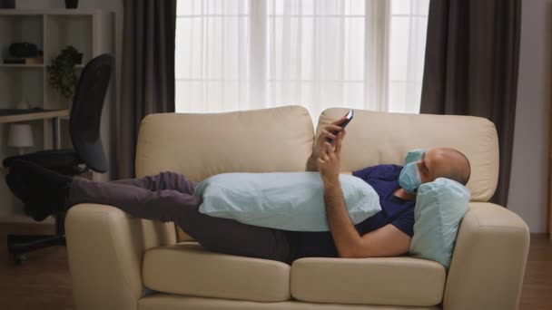 Unatkozó férfi védő maszkkal feküdt a kanapén — Stock videók