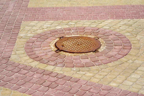Цветная плитка вокруг канализационного люка в парке — стоковое фото