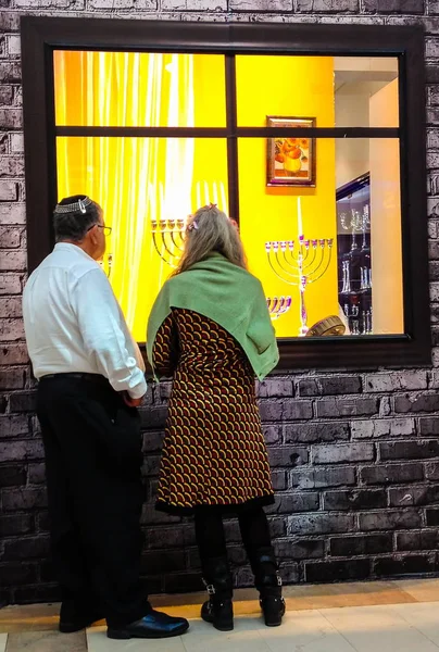 Tel Aviv, Israël - 22 December 2016: Bejaarde echtpaar op Showcase Judaïca opslaan voordat de vakantie van Hanukkah menorahs blootgesteld aan verschillende maten en modellen (traditionele kandelaar) — Stockfoto