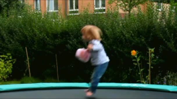 Pequeña linda chica rubia en el día de verano en el trampolín grande — Vídeos de Stock