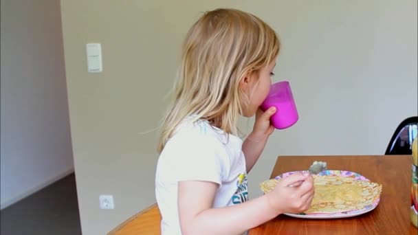 Niña comiendo panqueques y bebiendo leche en casa — Vídeos de Stock