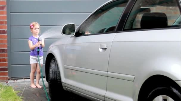 Маленькая босиком девушка помогает мыть машину из шланга с помощью спрея — стоковое видео