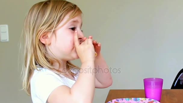 Niña vestida de blanco sentada en una mesa, comiendo panqueques y bebiendo leche en casa — Vídeos de Stock