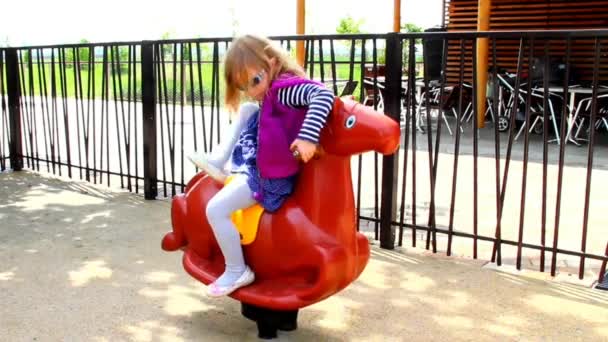 Kleines Mädchen reitet auf Schaukelpferd auf Kinderspielplatz — Stockvideo