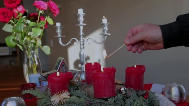 Homem idoso acende velas de Natal decorativas vermelhas em uma mesa de madeira — Vídeo de Stock