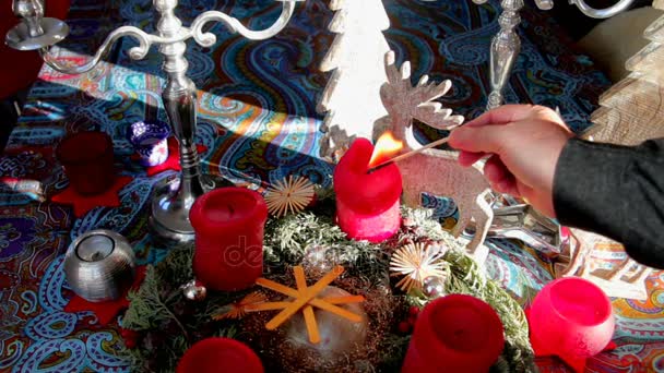Älterer Mann zündet rote dekorative Weihnachtskerzen auf einem Tisch an, auf dem eine farbige Tischdecke liegt — Stockvideo
