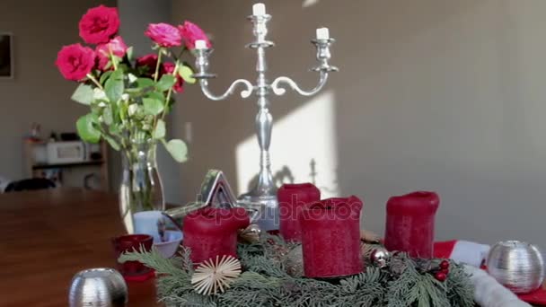 Weihnachtliche Installation eines Rosenstraußes in einer Glasvase, eines silbernen Leuchters und roter Dekorkerzen auf einem Holztisch — Stockvideo