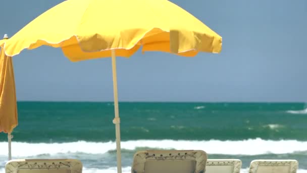 Жовтий пляжна парасолька та шезлонги на пляжі. Вибірковий фокус. — стокове відео