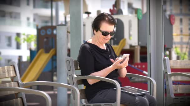 Oma met een Tablet en Smartphone op een bankje — Stockvideo