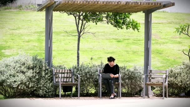 Starsza pani siedzi na ławce i używa jej na komputerze typu Tablet i smartfon w parku miejskim w słoneczny letni dzień. — Wideo stockowe