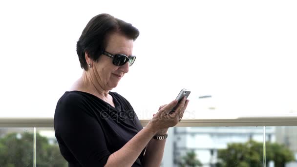 Старшая женщина со смартфоном на балконе — стоковое видео