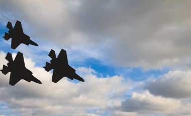 Mavi gökyüzü ve beyaz bulutlar karşı üç F-35 uçaklarının siluetleri