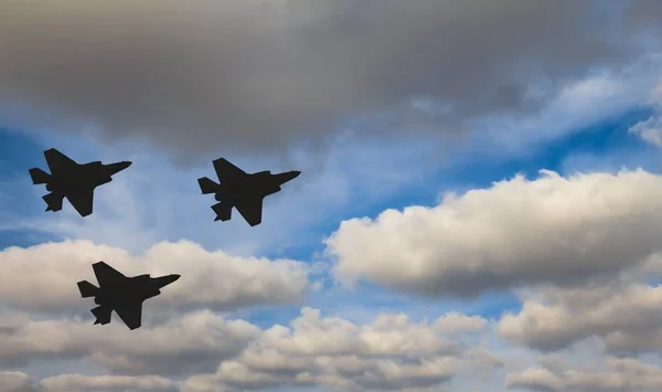 Siluetas de tres aviones F-35 contra el cielo azul y las nubes blancas —  Fotos de Stock