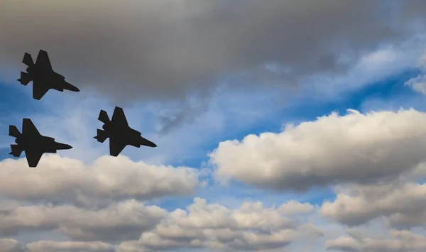 Siluetas de tres aviones F-35 contra el cielo azul y las nubes blancas — Foto de Stock