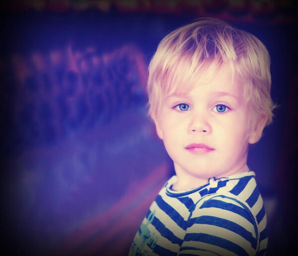 Two year blond old boy with blue eyes in a striped T-shirt on an abstract background