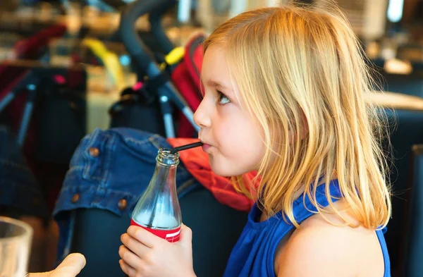 Menina loira de seis anos no restaurante bebendo um refrigerante — Fotografia de Stock