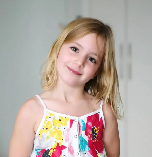 Niña rubia de seis años en un vestido blanco de verano con flores sonriendo sobre un fondo abstracto —  Fotos de Stock