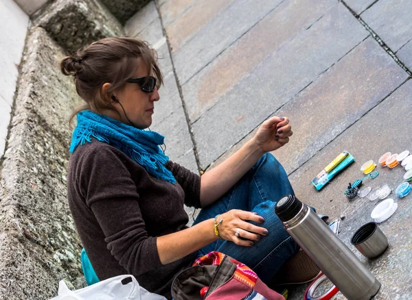 Jovem mulher sentada na calçada faz decorações bonitos de contas — Fotografia de Stock