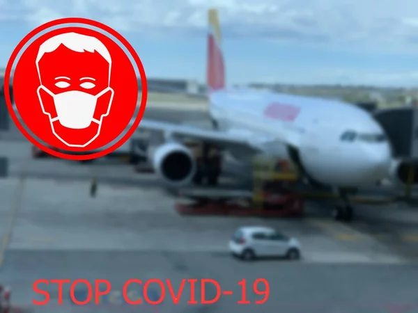 Stop COVID-19. Warning medical protection mask sign on airplane at one of the European airports background.