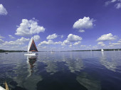 Segelboot auf einem schönen See bei blauem Himmel und angenehmer grüner Landschaft Hintergrund und schöne Reflexion auf der Wasseroberfläche. Segeln ist eine beliebte Sportart und Aktivität