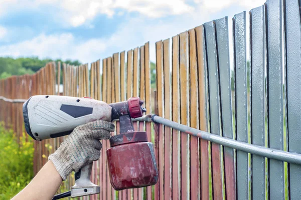 Painting metal fence spray. Man paints a fence with a paint sprayer. painting the fence to protect against corrosion