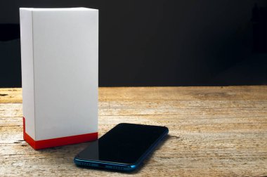 Tahta masadaki boş bir kutunun yanında yepyeni bir akıllı telefon.