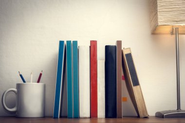 Tahta bir masanın üzerinde boş tahtası olan kitaplar renkli bir bardağın yanında.