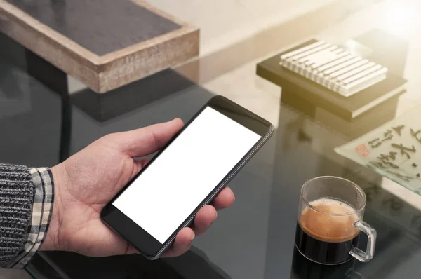 Homme tenir un smartphone écran vierge sur une table en verre avec une tasse — Photo