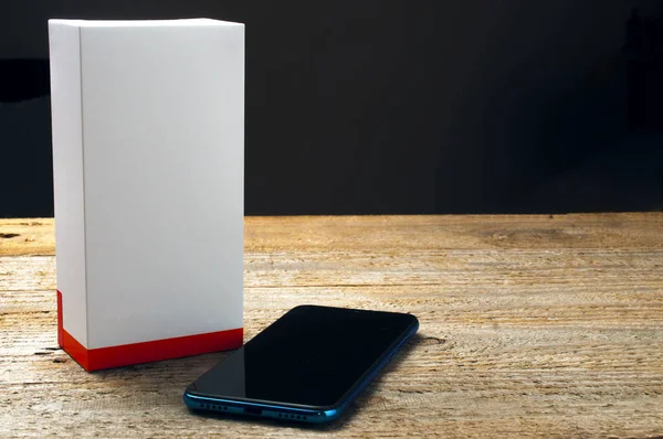 Brandneues Smartphone neben leerer Schachtel auf Holztisch — Stockfoto