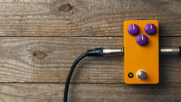 Blank orange guitar pedal with purple knobs and plugged jacks on