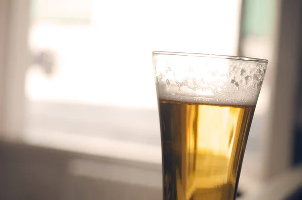 Sklenice zlatého piva s pěnou na rozmazaném pozadí, kinematografie — Stock fotografie
