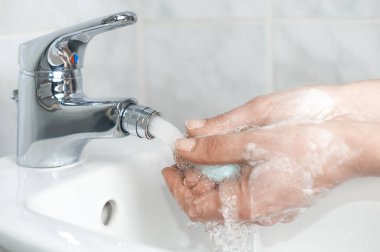Kadın elini musluğun altında akan suyla sabunluyor.