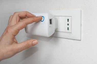 Kadın, duvar prizine takılı bir kablosuz yineleyiciyi açar