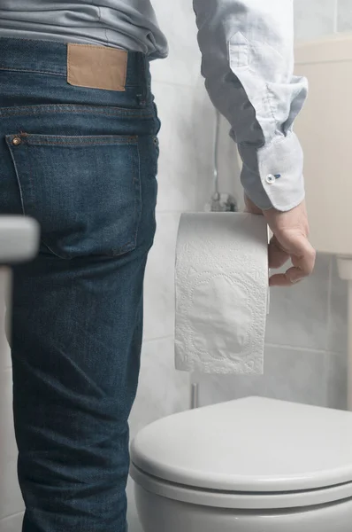 穿着斜纹棉布和衬衫的商人拿着一卷卫生纸在浴室里 — 图库照片