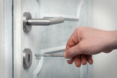Kafkasyalı bir adam eski paslı bir anahtar kullanarak modern bir kapı açar.