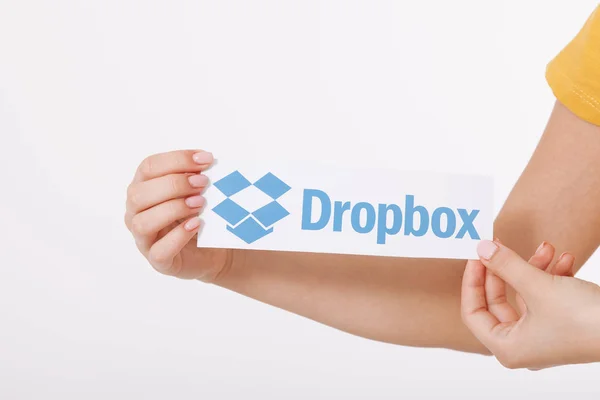 KIEV, UCRANIA - 22 de agosto de 2016: Manos de mujer con el logotipo de Dropbox impreso en papel sobre fondo blanco. Almacenamiento en la nube de Dropbox, que permite a los usuarios almacenar sus datos en servidores en la nube . — Foto de Stock