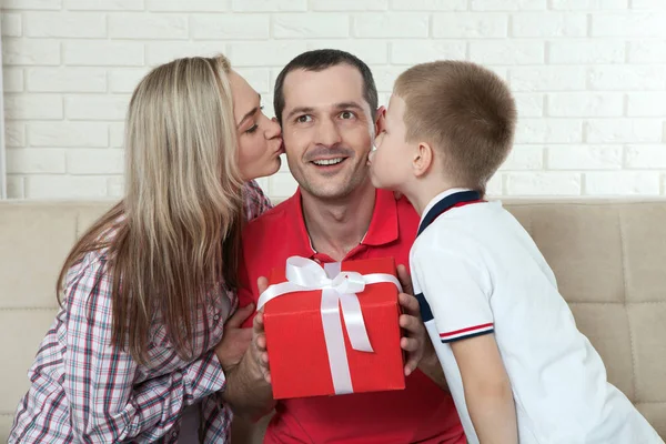 Father holding gift and receiving kisses from son and wife — Stock Photo, Image