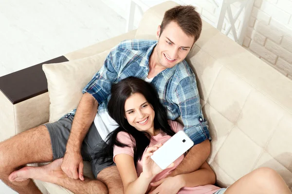 Feliz saludo de pareja casual en una videollamada telefónica en línea sentada en un sofá en la sala de estar en casa. Vista superior inusual . — Foto de Stock