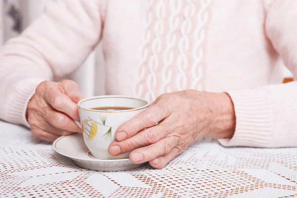 Una donna anziana beve tè a casa. Donna anziana che tiene una tazza di tè tra le mani a tavola primo piano — Foto Stock